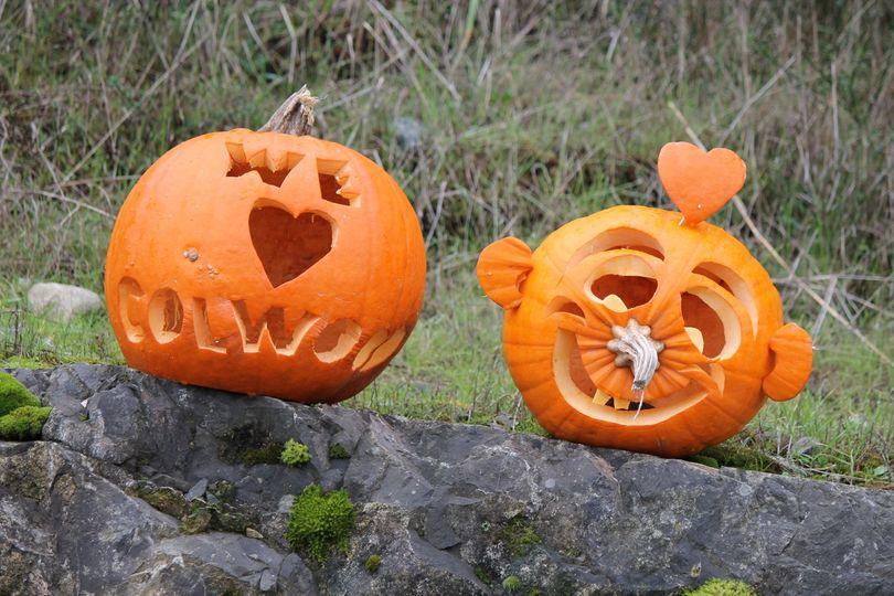 Two carved pumpkins on a rock, one with 'We ♥ Colwood' and the other with a smiling face and a heart-shaped nose.
