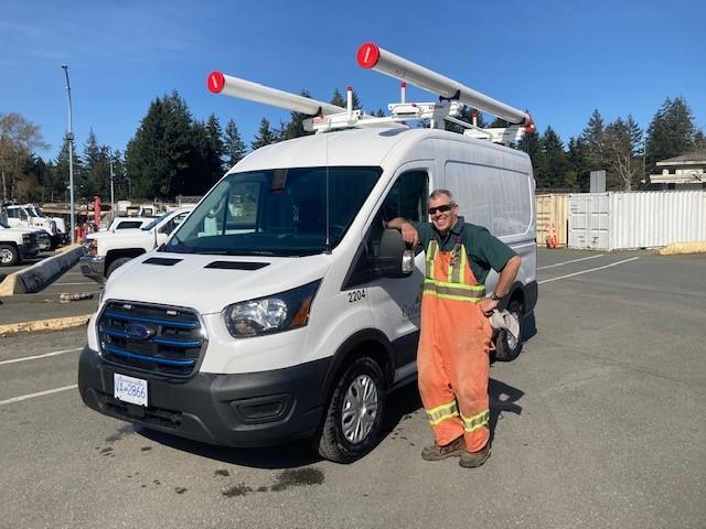 Utility worker in orange overalls posing next to a Colwood Zero Emission Fleet Vehicle.